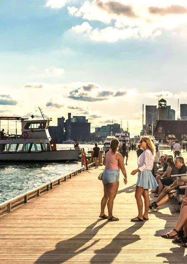 Tourist and locals having fun on a beach front pier with boats arriving in a late summer afternoon in Toronto ON.