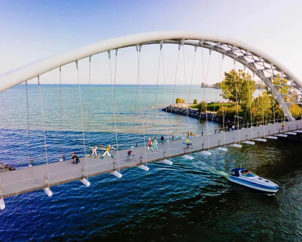 People, bikers on the Humber Arch Bridge, by Lake Ontario in Toronto, as sailboat passes beneath during the daytime.